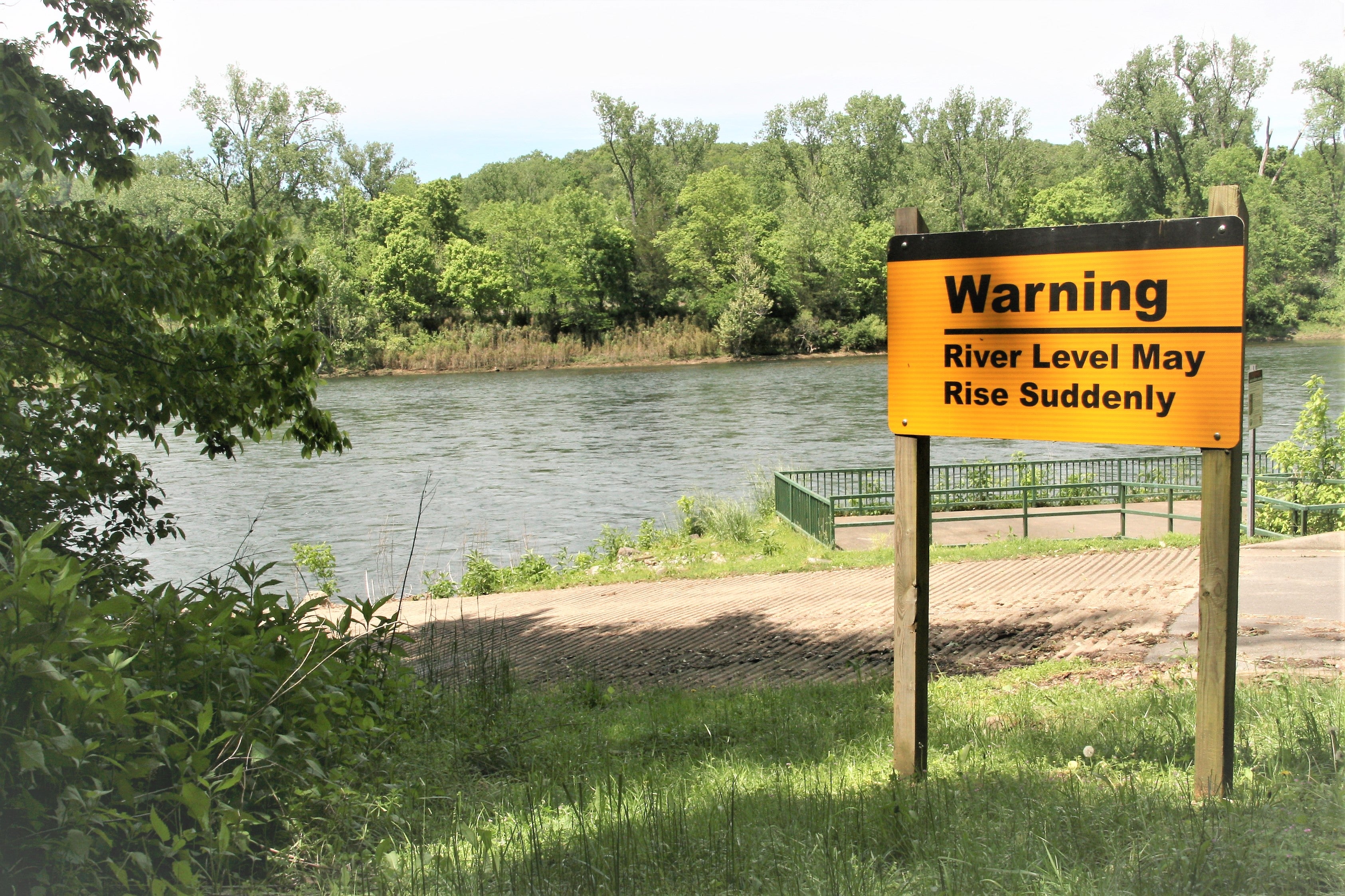 Large warning sign next to a river stating: Warning River Level May Rise Suddenly 